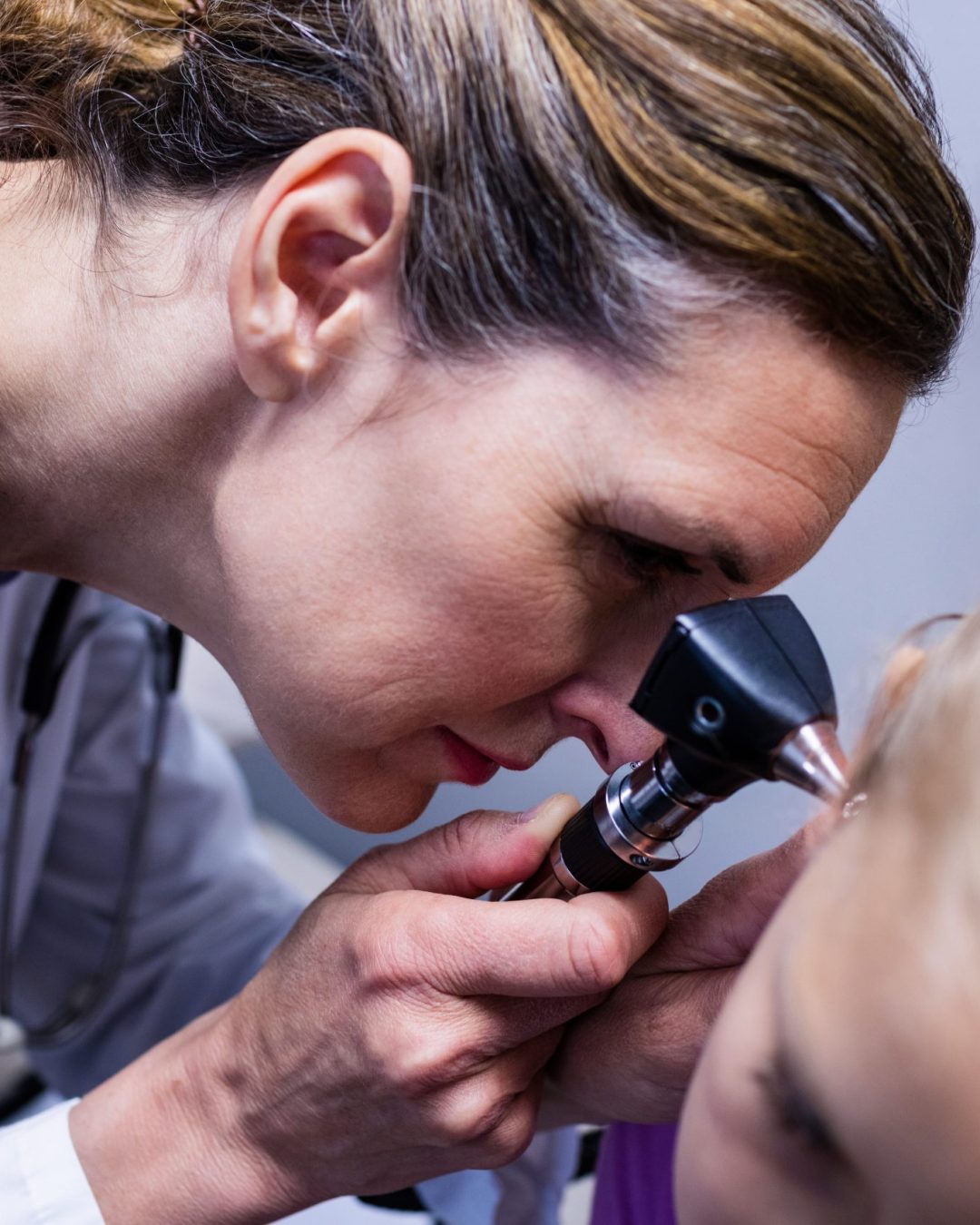 Female doctor examining patient ear with otoscope in hospital